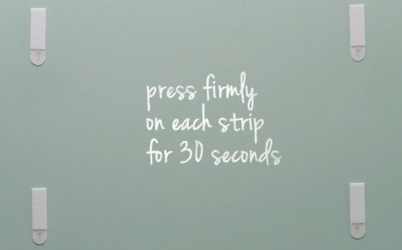 Remove frame and press each adhesive strips firmly on the wall.